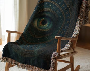 May include: A woven throw blanket featuring a large, detailed human eye centered within a circular frame. The design includes golden runic symbols and celestial constellations against a dark teal and black background, finished with fringed edges.