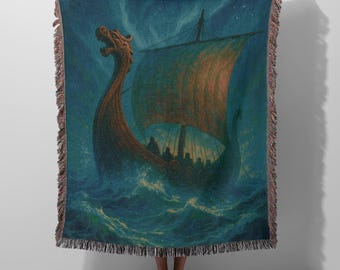 May include: A woven throw blanket featuring a dark blue and teal ocean scene with a wooden Viking longship. The ship has a carved dragon head prow and a large sail, navigating through choppy waves under a starry night sky, finished with fringe.