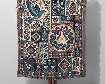 May include: A woven throw blanket featuring a patchwork design with a blue bird, a central Christmas wreath with a red bow, snowflakes, pinecones, and floral motifs in shades of navy blue, cream, red, and brown with a fringed edge.