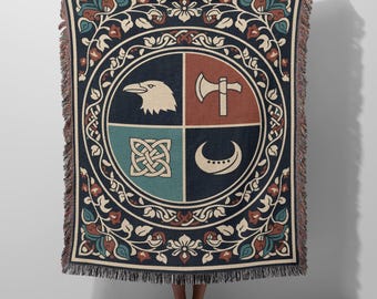 May include: A woven throw blanket featuring a dark blue background with a central circular emblem divided into four quadrants. The quadrants display a white eagle head, a white axe, a white Celtic knot, and a white crescent moon. The border has floral motifs.