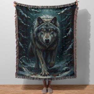 May include: A woven throw blanket featuring a detailed illustration of a wolf in a snowy forest. The wolf is depicted with gray and brown fur, amber eyes, and is walking towards the viewer. The blanket has a fringed edge.