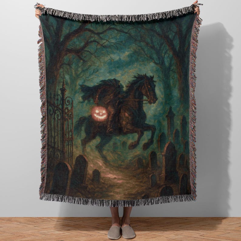 K&ouml;nnte beinhalten: Eine gewebte Wurfadecke mit einer gruseligen Illustration des kopflosen Reiters, der ein schwarzes Pferd durch einen Friedhof reitet. Das Kunstwerk hat eine dunkle, unheimliche Farbpalette mit einer K&uuml;rbislaterne.