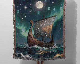 May include: A woven throw blanket featuring a dark night sky with a full moon, stars, and green aurora borealis. A wooden Viking ship with a sail displaying a constellation pattern floats on dark, churning ocean waves with white foam.