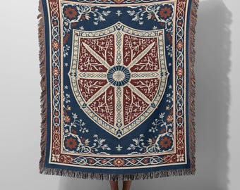 May include: A woven throw blanket featuring a large central shield emblem in deep blue, dark red, and cream. The design includes intricate floral vine borders and a fringed edge. The shield is divided into segments with stylized branch patterns.