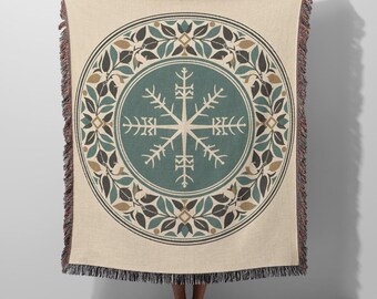 May include: A woven throw blanket featuring a cream-colored background with a large central teal circle. Inside the circle is a white geometric snowflake-like symbol. A decorative border of teal and brown leaves surrounds the central design.