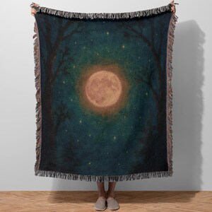 May include: A woven throw blanket featuring a nighttime forest scene. The design includes a large, glowing full moon, stars, and silhouetted trees against a dark teal background. The blanket has a fringed edge.