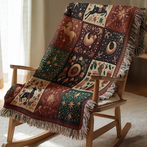 Puede incluir: Una manta tejida sobre una mecedora de madera. La manta presenta un diseño de patchwork con motivos celestiales y animales en tonos burdeos, verdes y crema. La manta tiene un borde con flecos.