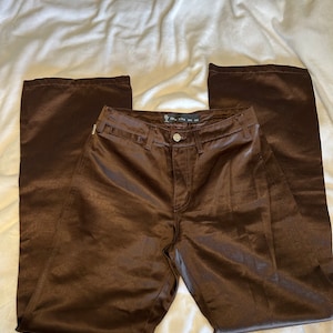 May include: A pair of brown satin pants with a zipper fly and button closure. The pants have a straight leg and a slightly flared hem.