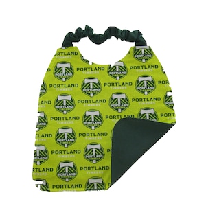 May include: A green and yellow baby bib with a repeating pattern of the Portland Timbers soccer team logo. The bib has a green fleece backing.