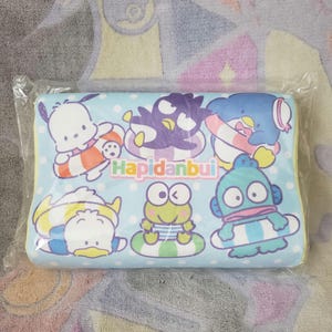May include: A rectangular pillow featuring cartoon characters in inner tubes on a light blue background with white polka dots. The text "Hapidanbui" is printed in green. The pillow is packaged in clear plastic.