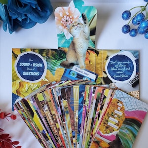 May include: A deck of "The Sound + Vision Deck of Questions" cards with a cat illustration and the text "BOWIE MIX". The cards have colourful, abstract designs. A card reads "may it produce a luminous impression".