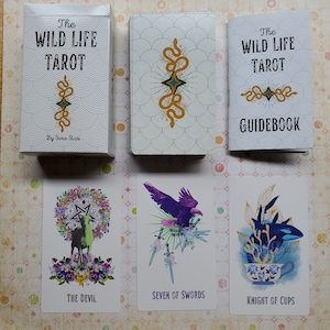 May include: The Wild Life Tarot deck and guidebook by Sara Stasi. The deck features colorful illustrations of animals and plants. The guidebook is white with green and gold accents.