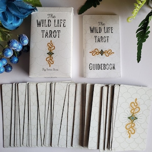 May include: A deck of The Wild Life Tarot cards with a guidebook. The cards have a white background with a black and white pattern of overlapping circles. The guidebook has a white background with a black and white pattern of overlapping circles and the text "The Wild Life Tarot Guidebook".