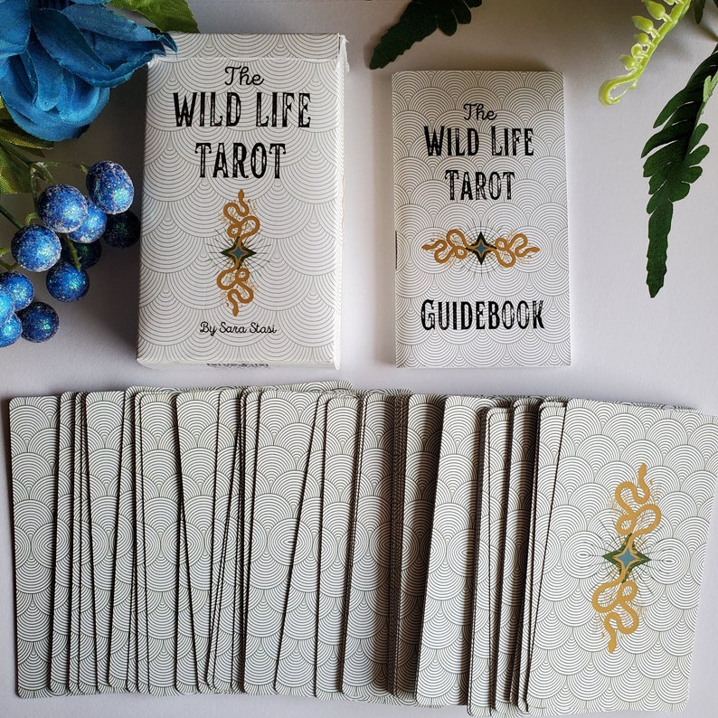 May include: A deck of The Wild Life Tarot cards with a guidebook. The cards have a white background with a black and white pattern of overlapping circles. The guidebook has a white background with a black and white pattern of overlapping circles and the text "The Wild Life Tarot Guidebook".