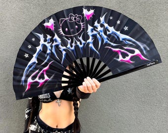May include: Black folding hand fan with a design featuring a Hello Kitty character, pink hearts, and blue and pink flame-like accents. The fan has a black frame and is held open.