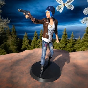 Può includere: Una action figure di una donna con i capelli blu che tiene una pistola. Indossa una giacca di pelle marrone, jeans blu e una maglietta bianca con un design a forma di teschio. La figura è in piedi su una base nera.