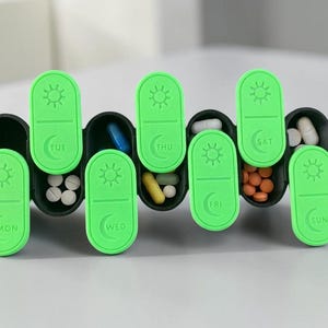 May include: A weekly pill organiser with seven compartments, each labelled with a day of the week in green. The compartments are black and contain various pills and capsules. The lids are green with a sun symbol.