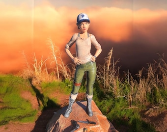 May include: A figurine of a young woman wearing a blue baseball cap, a light brown shirt, and green pants. She is standing on a rock with a brown background.