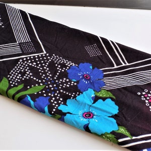 May include: Black fabric with a geometric pattern of white lines and squares. The fabric is decorated with blue and green flowers.