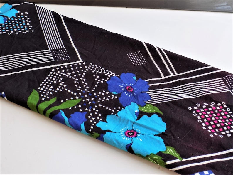 May include: Black fabric with a geometric pattern of white lines and squares. The fabric is decorated with blue and green flowers.