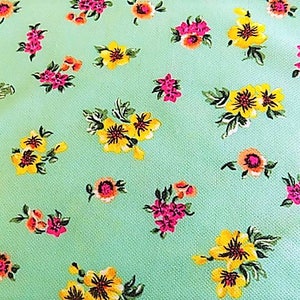 May include: A mint green fabric with a repeating pattern of small pink and yellow flowers. The fabric has a subtle texture.