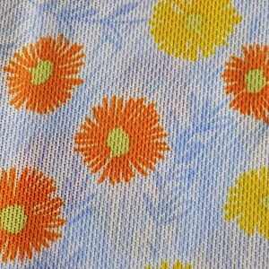 May include: White fabric with a repeating pattern of orange and yellow flowers. The flowers have a yellow center and orange petals.