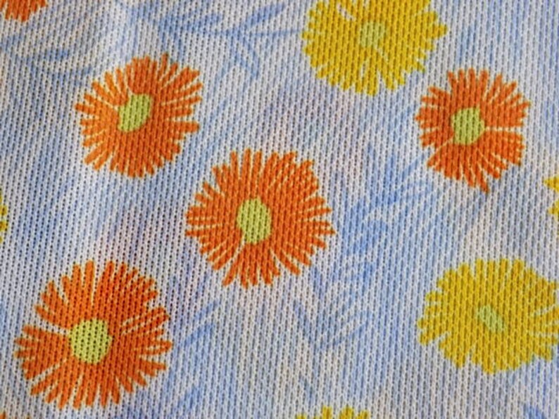 May include: White fabric with a repeating pattern of orange and yellow flowers. The flowers have a yellow center and orange petals.