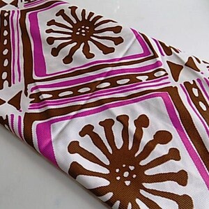 May include: White fabric with a geometric pattern in brown and pink. The pattern features stylized flowers and squares.