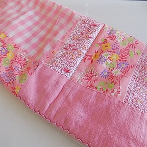 May include: A pink patchwork quilt with floral and gingham patterns. The quilt is made of different fabrics sewn together to create a unique design.