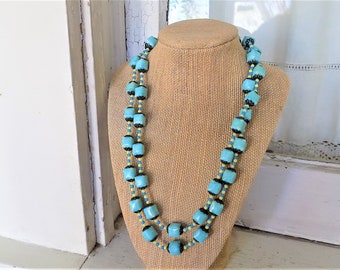 Op de afbeelding: Een dubbele ketting van vierkante kralen in turquoise blauw, zwart en geel.