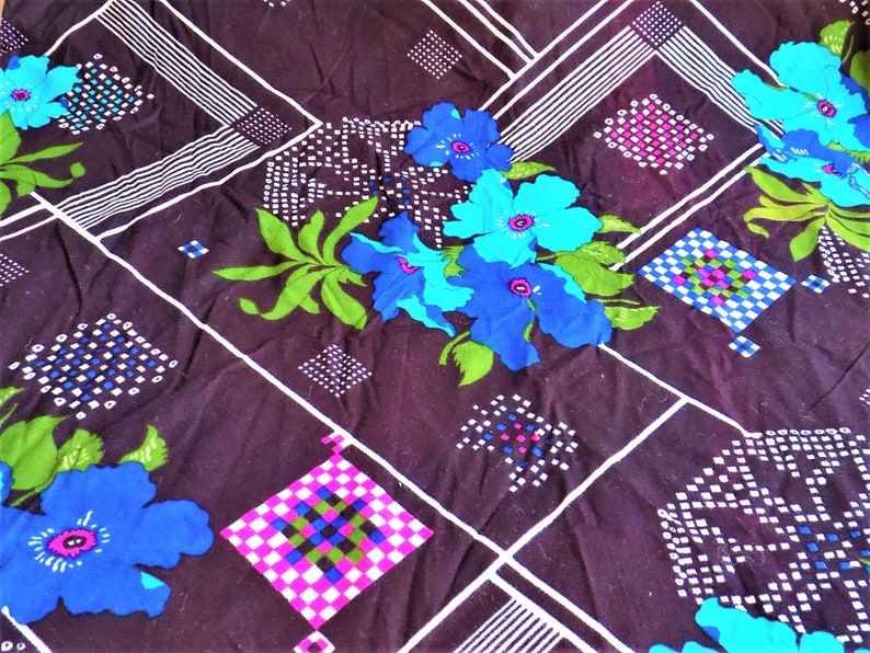 May include: A dark brown fabric with a geometric pattern of white and black lines, white and black squares, and white and black dots. The fabric also features a floral pattern with blue, green, and purple flowers.