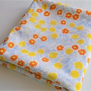 May include: A folded piece of fabric with a white background and a repeating pattern of orange and yellow flowers.