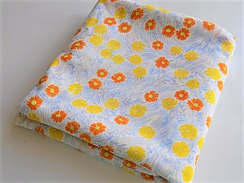 May include: A folded piece of fabric with a white background and a repeating pattern of orange and yellow flowers.