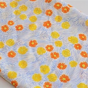 May include: A white fabric with a repeating pattern of yellow and orange flowers. The flowers are stylized and have a simple design.
