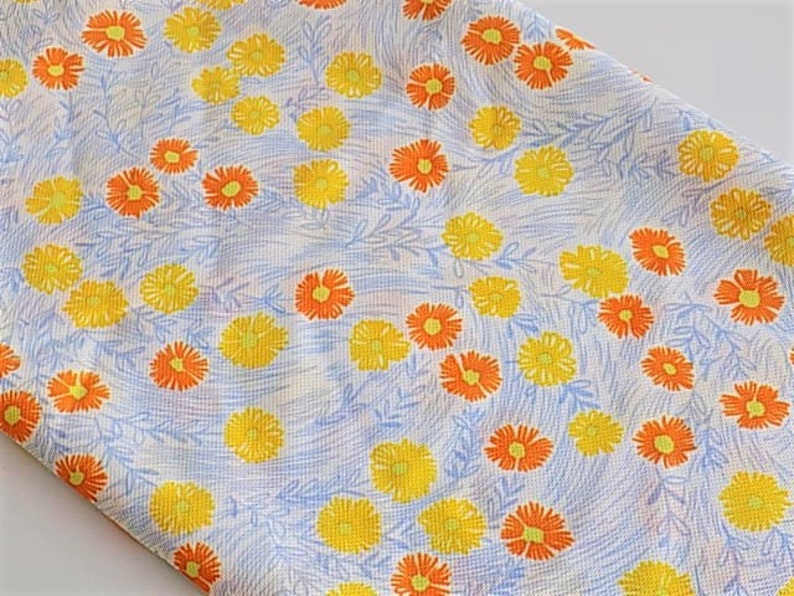 May include: A white fabric with a repeating pattern of yellow and orange flowers. The flowers are stylized and have a simple design.