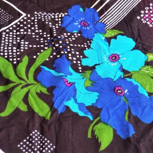 May include: A black fabric with a geometric pattern and blue and green floral design. The flowers are stylized and have a retro feel.