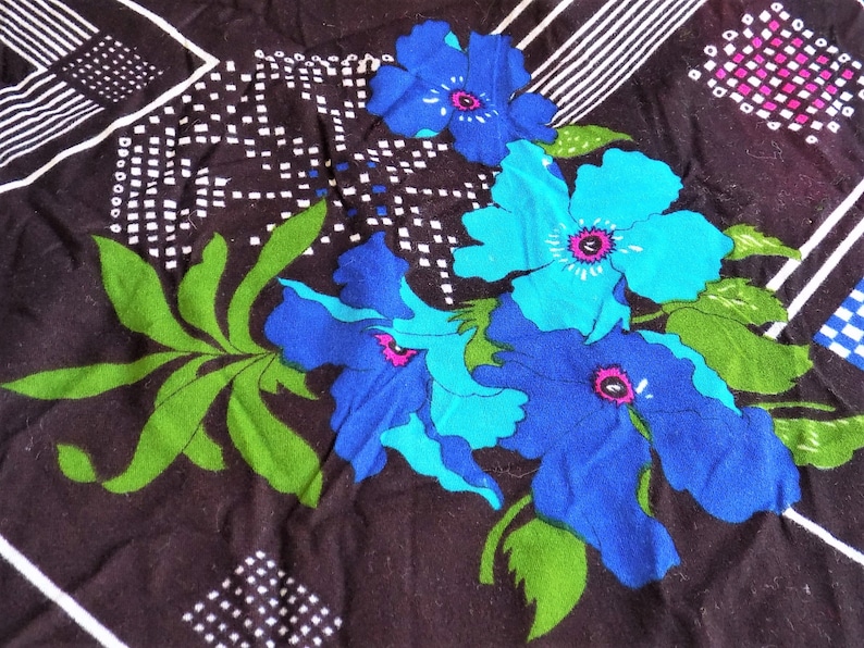 May include: A black fabric with a geometric pattern and blue and green floral design. The flowers are stylized and have a retro feel.