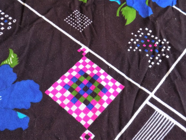 May include: Black fabric with a white, pink, blue, and green checkered pattern. The fabric also has a white and black geometric pattern and a blue flower.