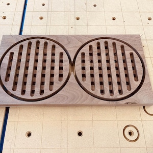 Puede incluir: Dos posavasos redondos de madera con un patrón de rejilla cortado. Los posavasos están conectados en el medio y están hechos de madera de nogal.