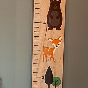 May include: Wooden family growing board with woodland animal illustrations. Features an owl, raccoon, fox, bear, deer, squirrel, rabbit, and mushroom. Includes measurements in inches and the text "Family Growing Board" and "Loved Beyond Measure".