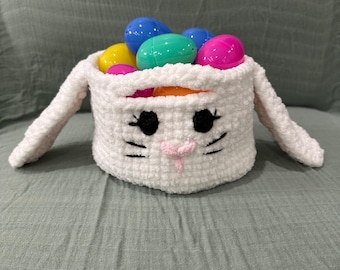 May include: White crocheted bunny basket filled with colorful plastic Easter eggs. The basket has black eyes, a pink nose, and a black stitched mouth.