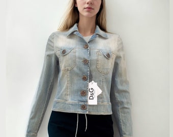 Op de afbeelding: Een lichtblauw denim jack met een wit label met de tekst "D&G" dat aan de knoop hangt. Het jack heeft een knoopsluiting en twee borstzakken.
