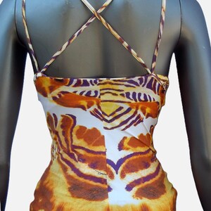 Op de afbeelding: Een mouwloze camisole met een levendig tijgerstrepenpatroon in tinten oranje, geel, wit en dieppaars. Het kledingstuk heeft dunne, kruisende schouderbandjes die een X-vorm op de rug vormen en een rechte zoom aan de onderkant.