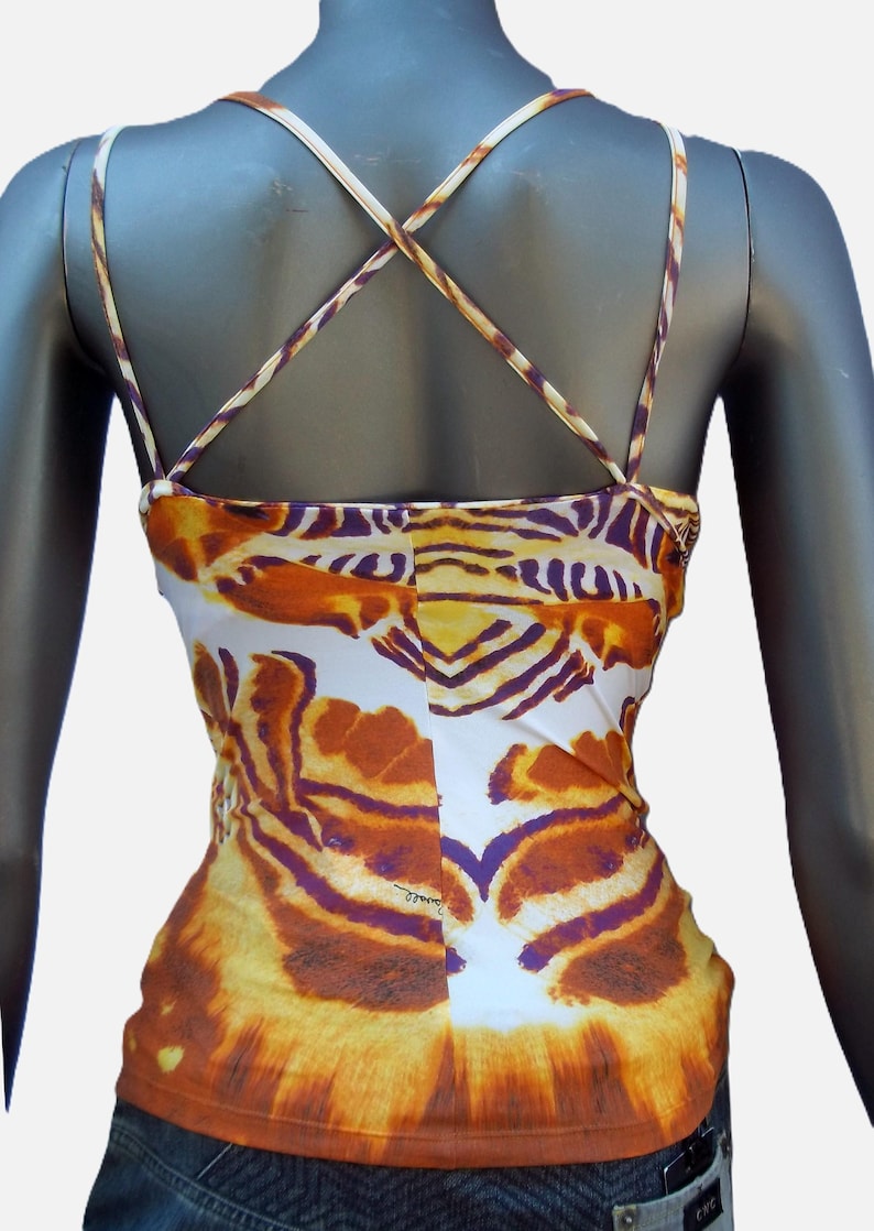 Op de afbeelding: Een mouwloze camisole met een levendig tijgerstrepenpatroon in tinten oranje, geel, wit en dieppaars. Het kledingstuk heeft dunne, kruisende schouderbandjes die een X-vorm op de rug vormen en een rechte zoom aan de onderkant.