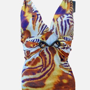 Op de afbeelding: Een mouwloze top met een levendig tijgerstrepenpatroon in tinten oranje, geel, wit en donkerpaars. Het kledingstuk heeft een diepe V-hals en een centraal zwart decoratief element dat de stof bij de taille samenbrengt.