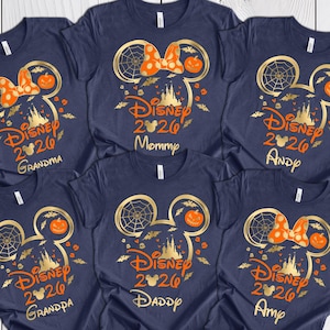 May include: Six navy blue short-sleeve t-shirts featuring a gold and orange graphic of a Mickey Mouse silhouette, a spider web, a pumpkin, and a castle. The text reads Disney 2026 with names Grandma, Mommy, Andy, Grandpa, Daddy, and Amy printed below.