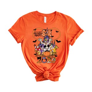 May include: An orange short-sleeve t-shirt featuring a graphic of Disney characters in Halloween costumes, a castle, bats, and the text "NOT SO SCARY HALLOWEEN PARTY!" and "2020" with a Minnie Mouse bow icon above the characters.