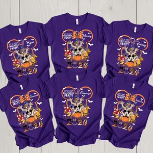 May include: Six purple short-sleeve t-shirts featuring a graphic of Disney characters in front of a castle. The design includes a Mickey Mouse ear outline, the text Not So Scary Halloween Party, and the year 2026 with individual names printed.