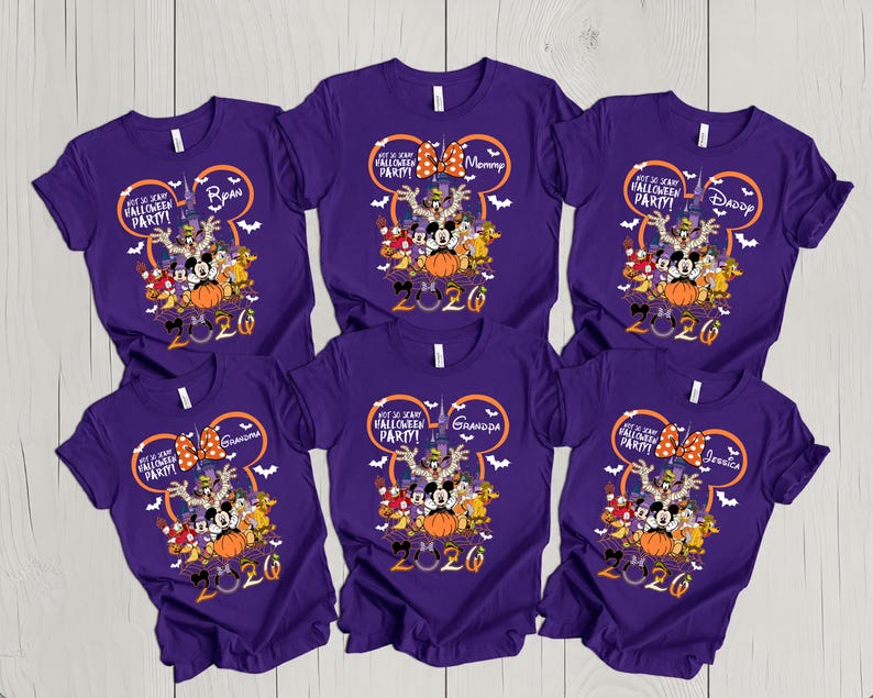 May include: Six purple short-sleeve t-shirts featuring a graphic of Disney characters in front of a castle. The design includes a Mickey Mouse ear outline, the text Not So Scary Halloween Party, and the year 2026 with individual names printed.