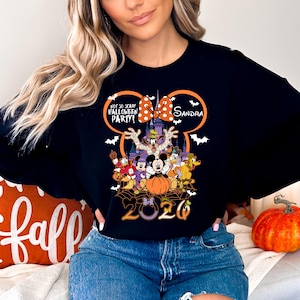 May include: A black long-sleeve sweatshirt featuring a graphic of Disney characters in Halloween costumes, a castle, and the text "Not So Scary Halloween Party!" with a personalized name "Sandra" and the year "2020" inside a Mickey Mouse ear outline.
